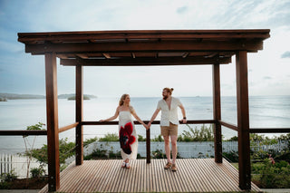 Photograph of a couple holding hands under a cabana looking out to the ocean