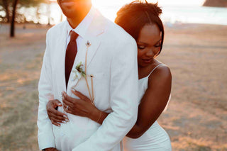 Photograph of a bride and groom on the beach. The bride is embracing the groom and the DreamArt photographer has focused on her dainty wedding jewellery.