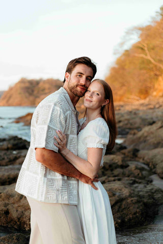 Photograph of an engaged couple posing by the rocks on the beach, taken by a DreamArt photographer
