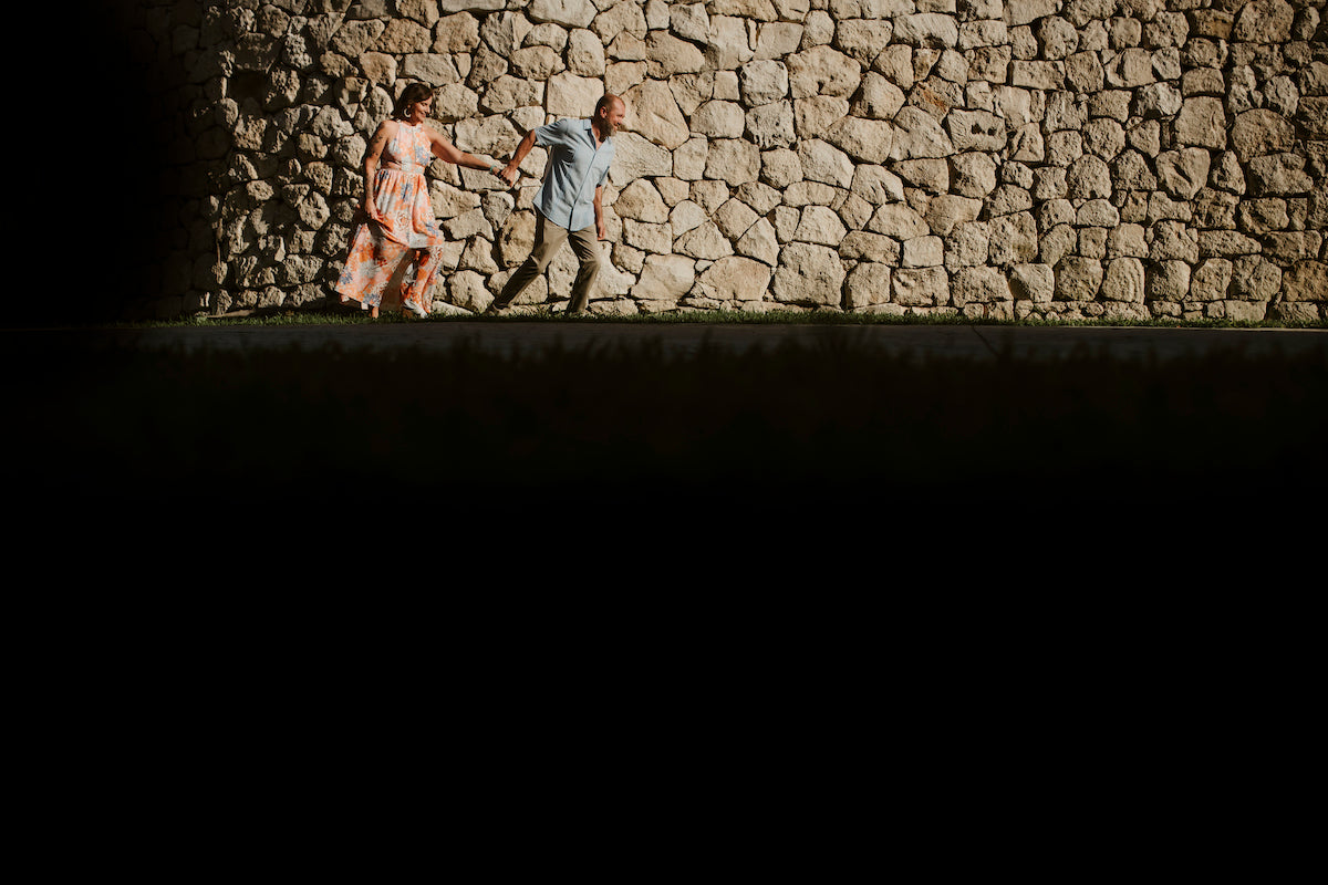 Couple runs hand in hand past a sunlit stone wall at Valentin Imperial Riviera Maya