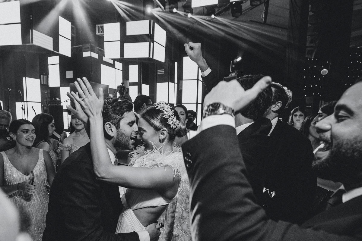 Bride in a crystal crown dances with the groom among cheering guests at a black and white reception