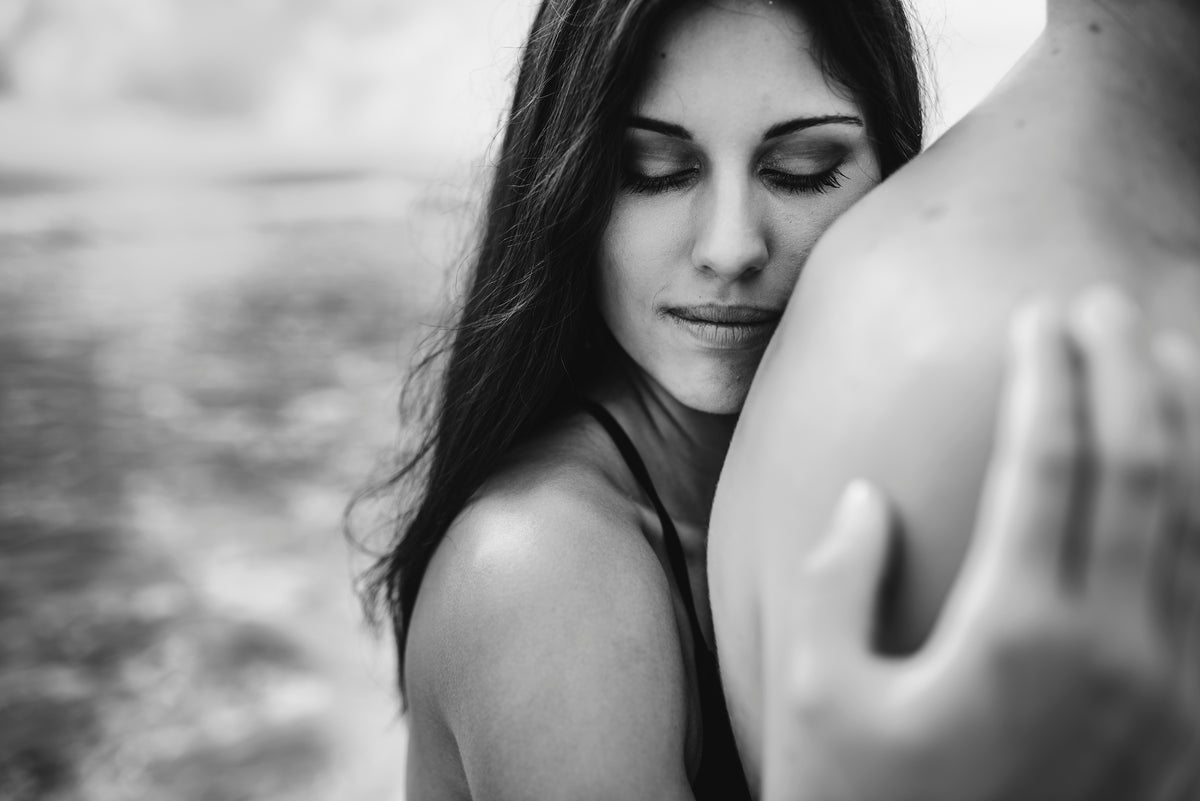 Black-and-white close-up of a woman resting her head on a man's shoulder outdoors