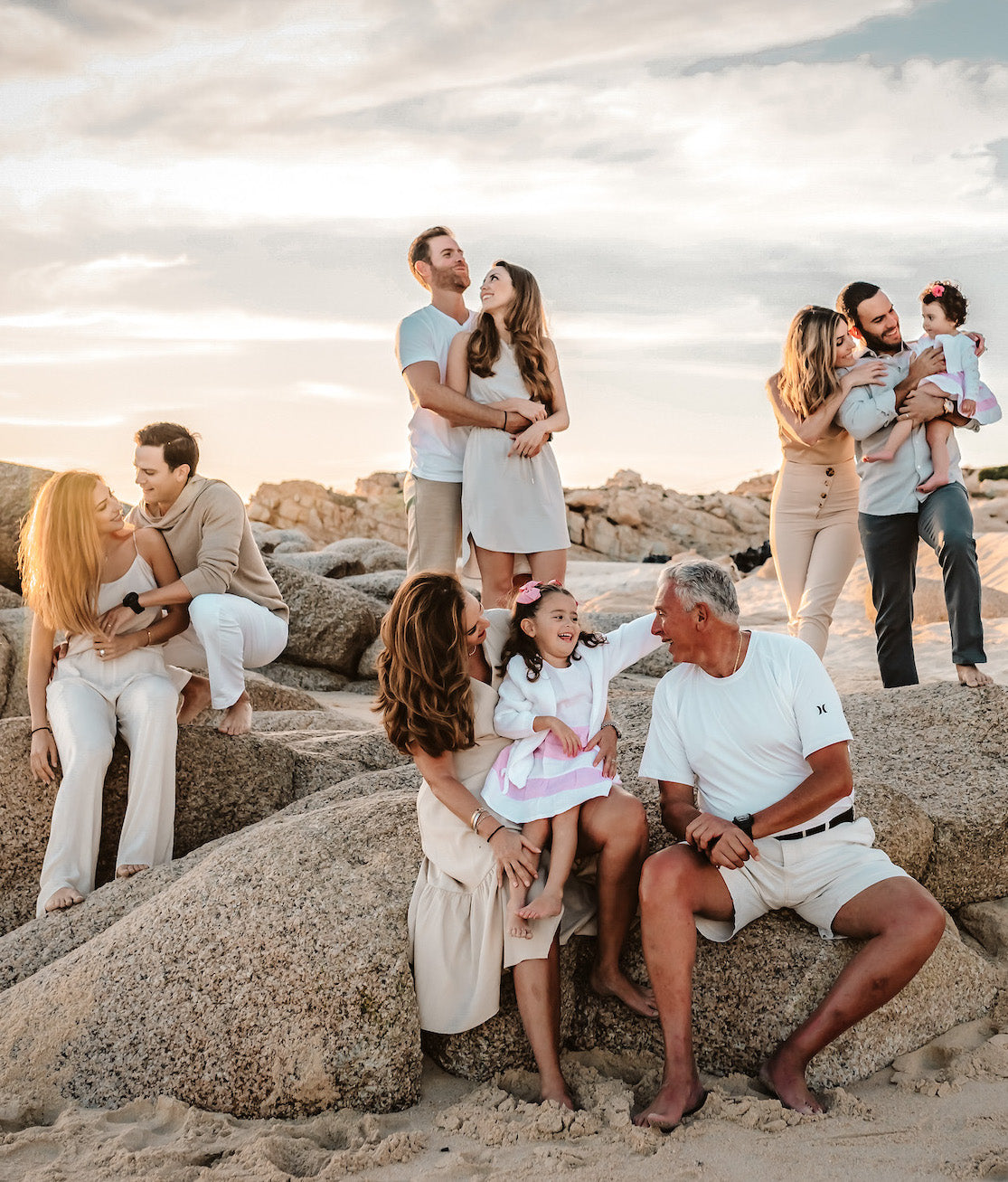 Three generations of a family sit together on granite boulders on the beach at sunset