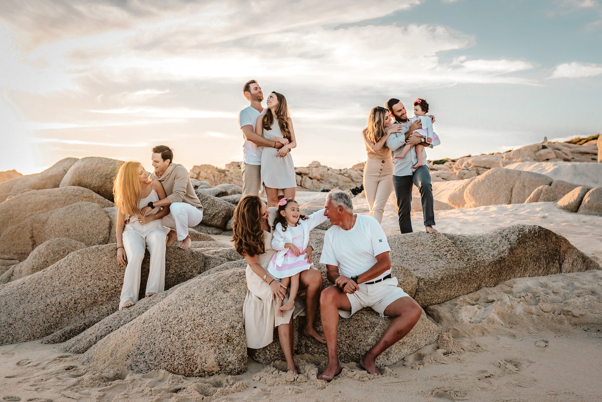 Wide shot of an extended family with grandparents and grandchildren gathered on beach rocks at golden hour