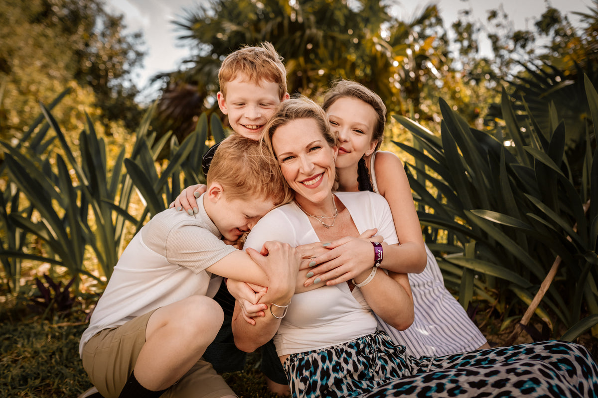 Mom hugged tightly by her three children among tropical plants during a family vacation photoshoot