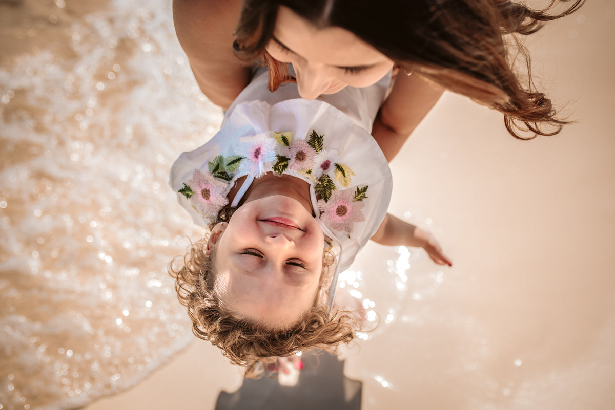Mother holds her curly-haired daughter upside down above the waves in a playful overhead beach shot