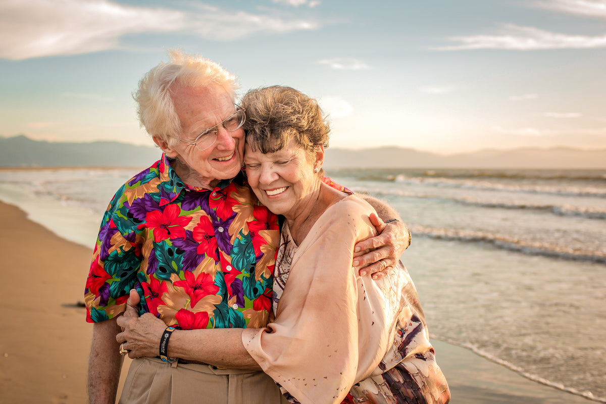 Senior couple hugging cheek to cheek on the beach at golden hour during a couples photoshoot