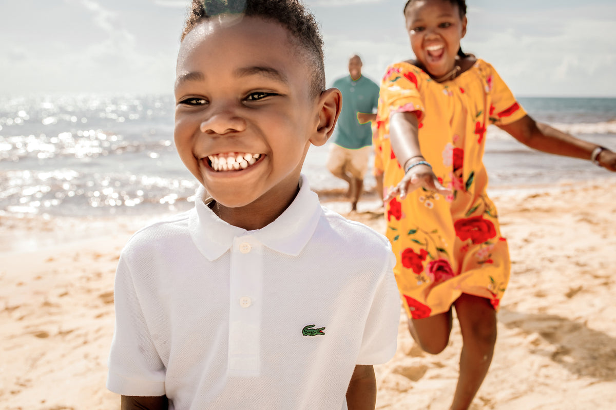 Grinning boy runs on the sand ahead of his sister and dad during a family beach photoshoot