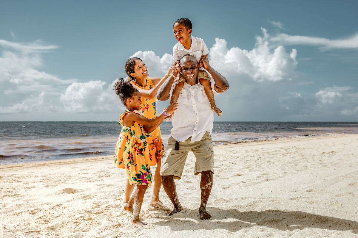 Family laughing on the beach with a boy on his father's shoulders during a family photoshoot