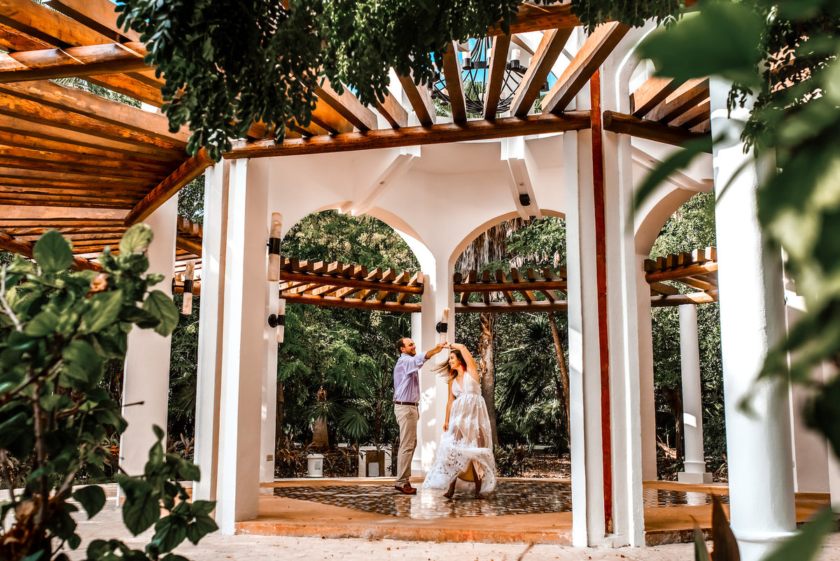 Groom spins his bride beneath a white pergola in the jungle at Valentin Imperial Riviera Maya
