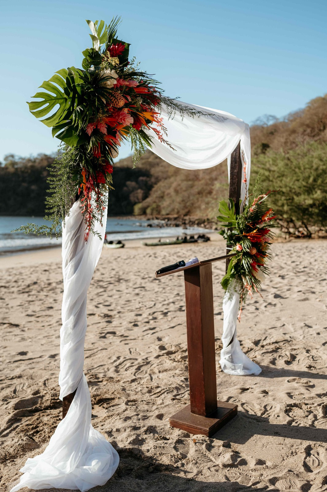 Photograph of a beach wedding arch decorated with big flowers, captured by a DreamArt photographer