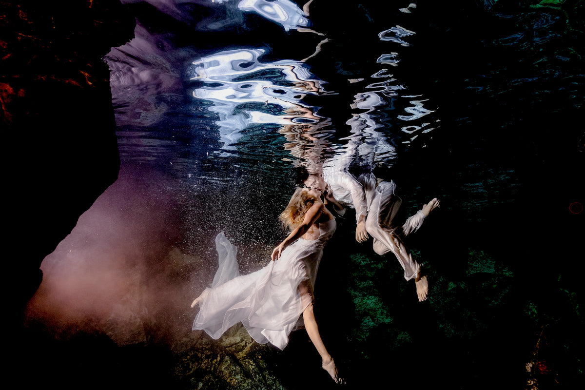Underwater wedding portrait of a bride and groom drifting together beneath the surface of a dark cenote