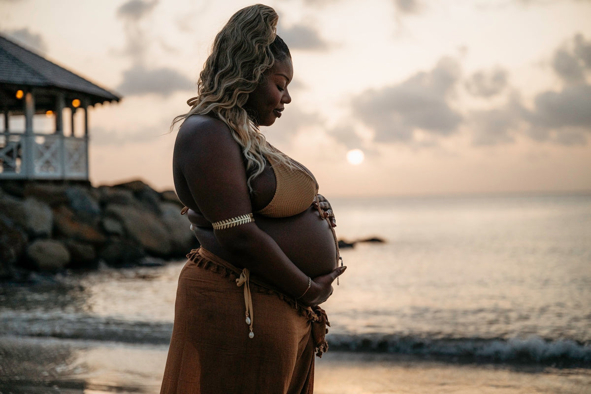 Photograph of a soon-to-be mother holding her baby bump at the beach