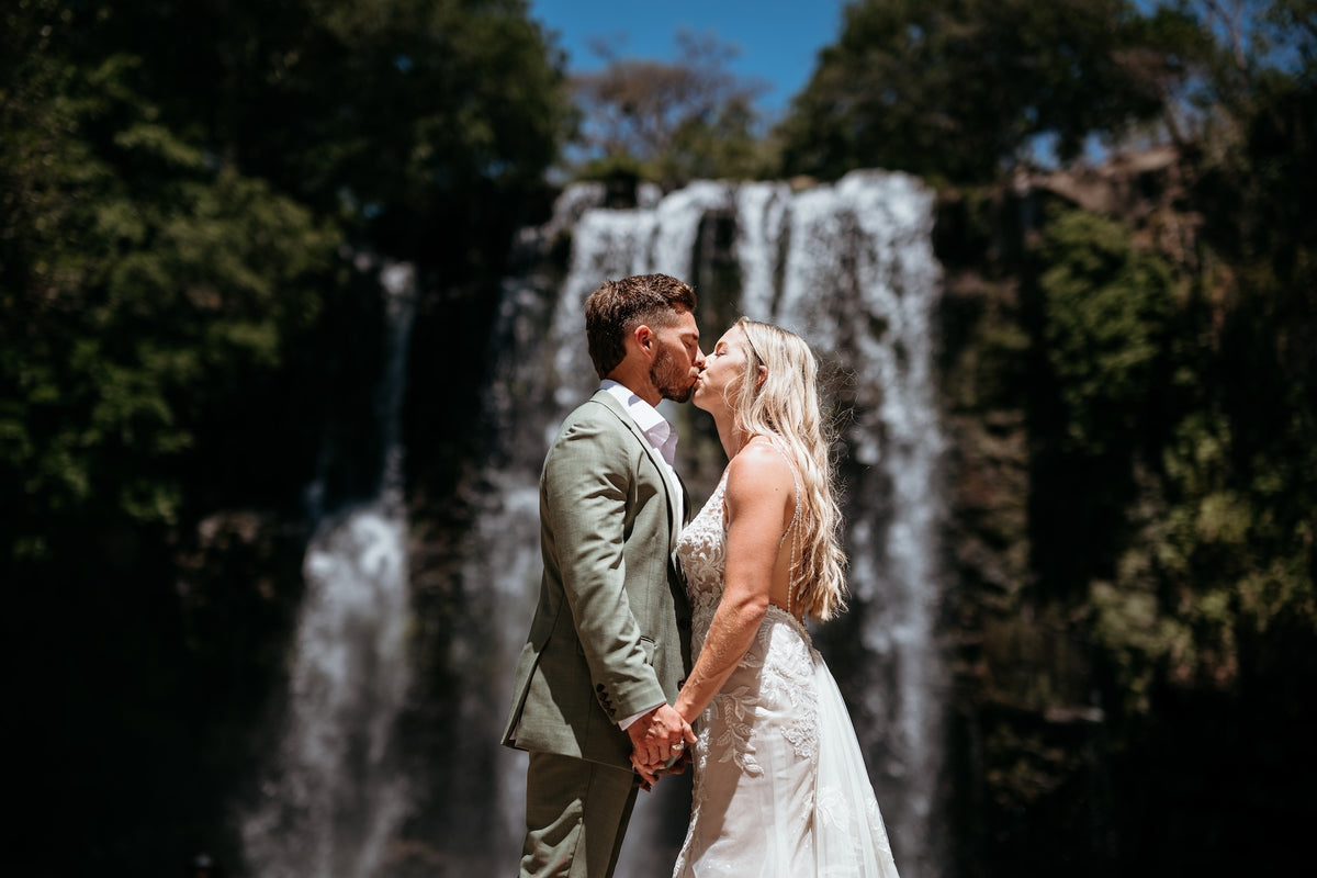 Photograph of a bride and groom kissing in front of a Costa Rican waterfall, captured by a DreamArt Photographer for a Trash Photoshoot