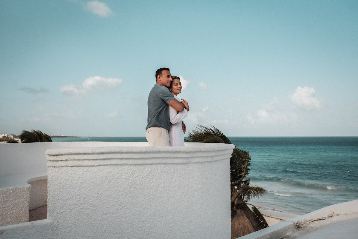Couple embraces on a white rooftop terrace overlooking the Caribbean at Belmond Maroma