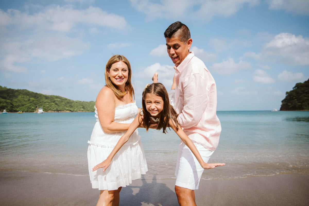 Photograph of parents holding their child as they are photographed on the beach by a DreamArt Photographer
