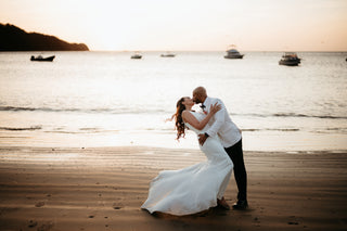 wedding couple kissing in the beach with a sunset and boat at the back 