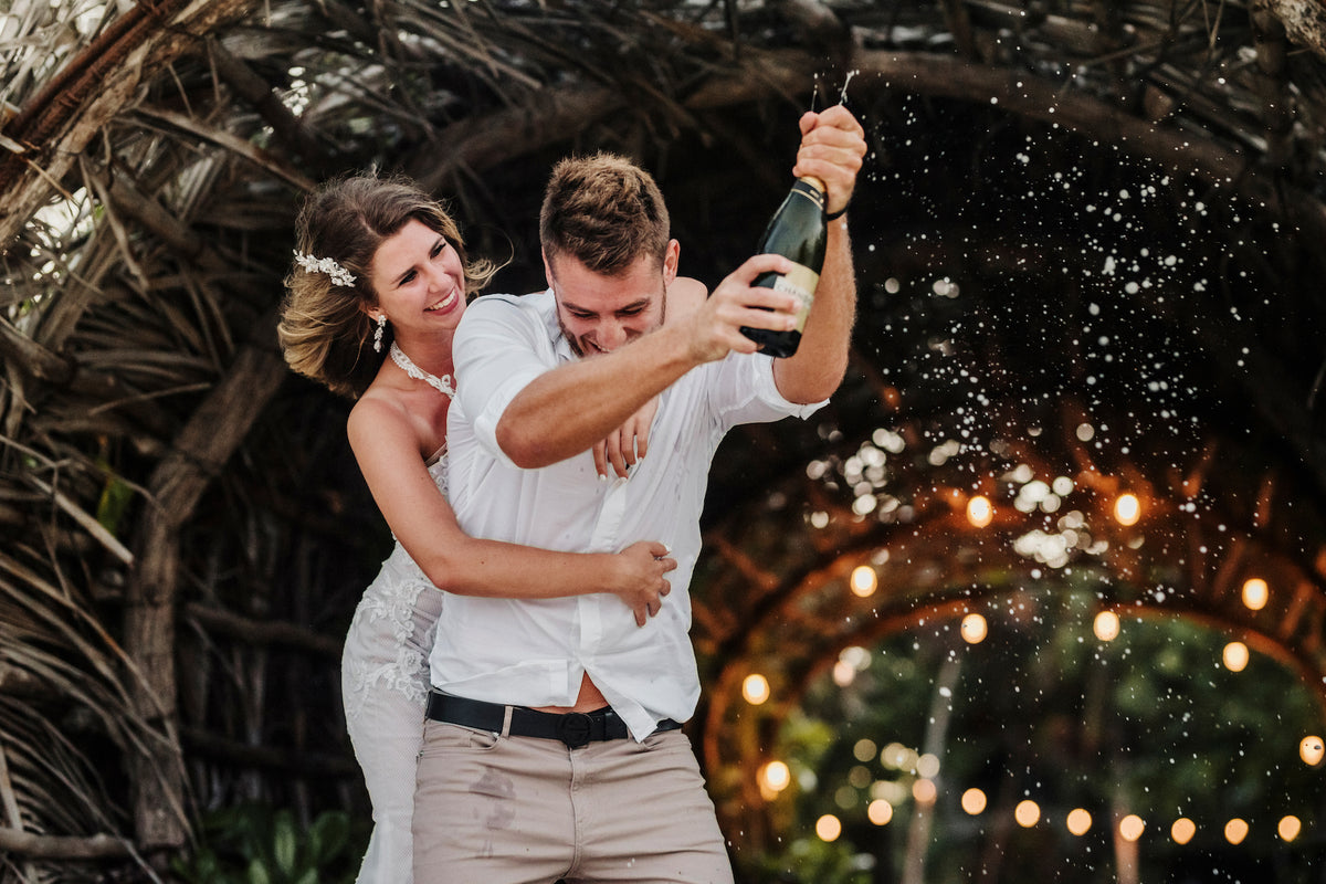 Groom sprays champagne as the bride hugs him under a woven arch at their Casa Malca Tulum wedding