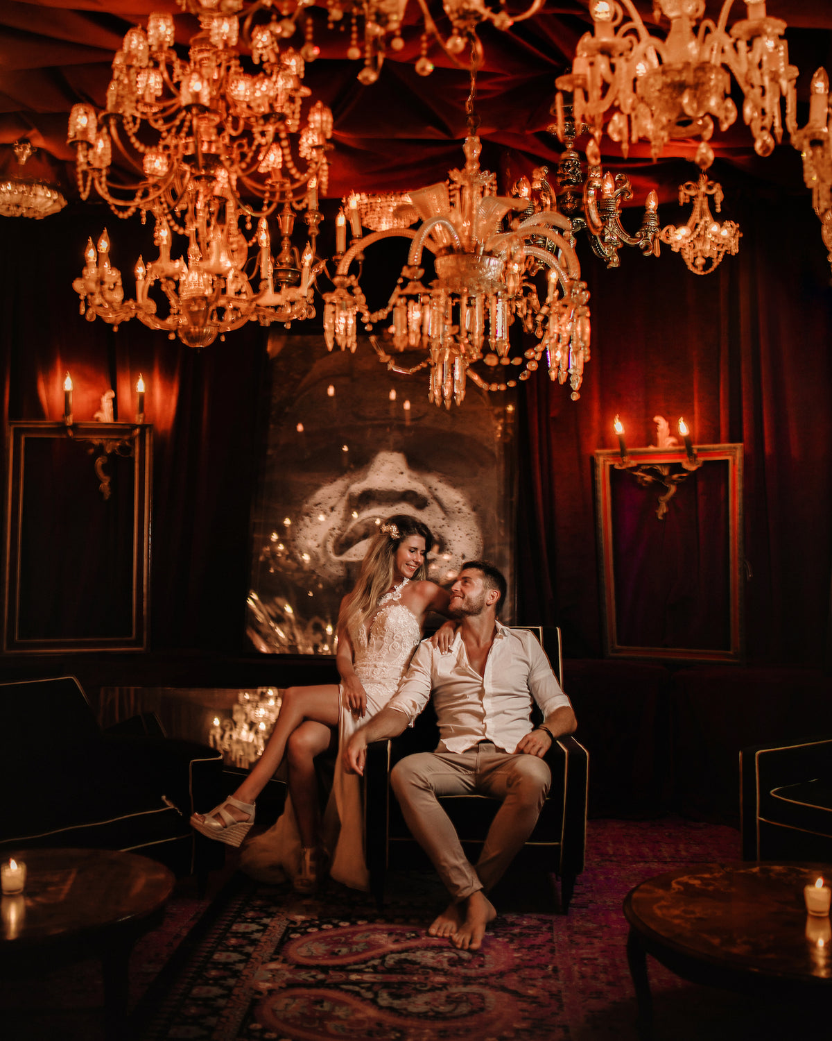 Couple share a smile in a candlelit lounge beneath crystal chandeliers at Casa Malca Tulum