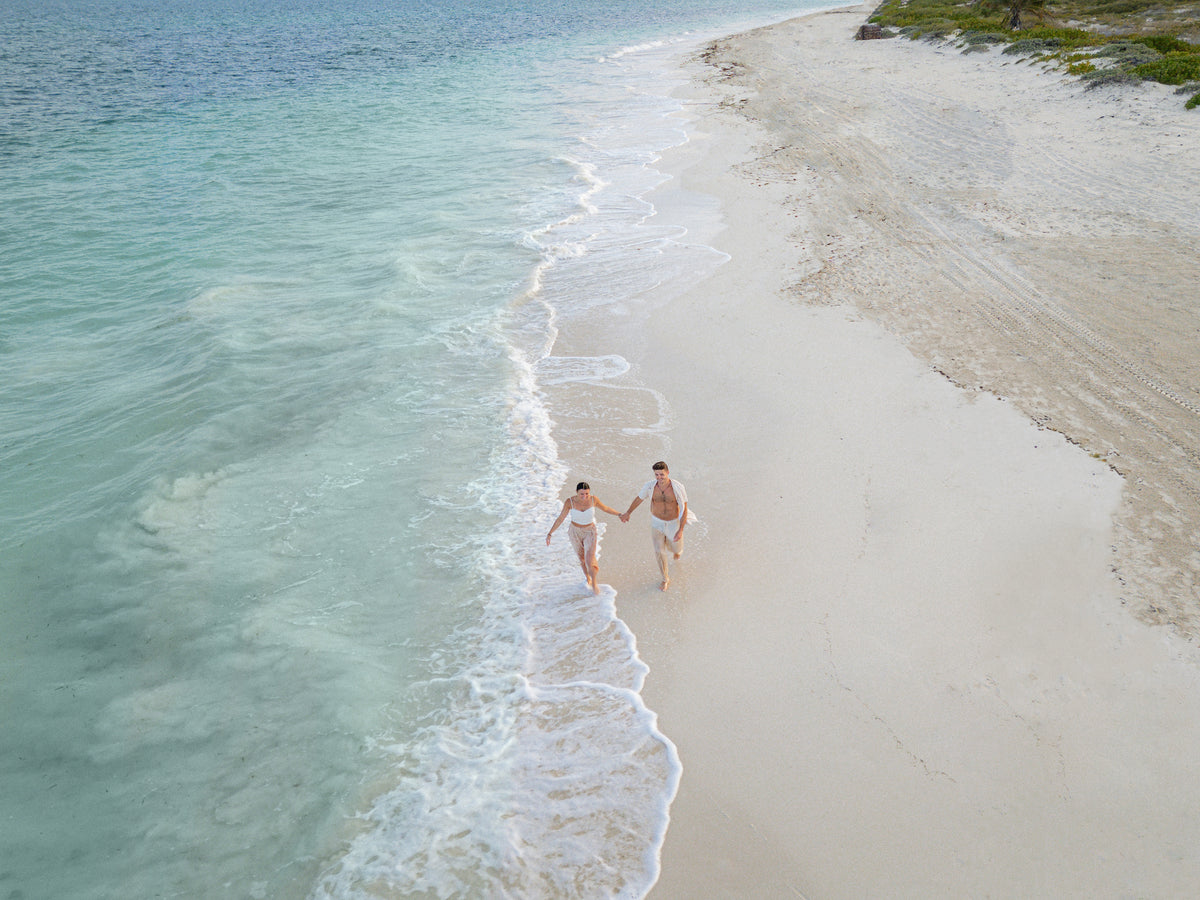 Drone view of a couple walking hand in hand along the shoreline at Dreams Las Mareas Costa Rica