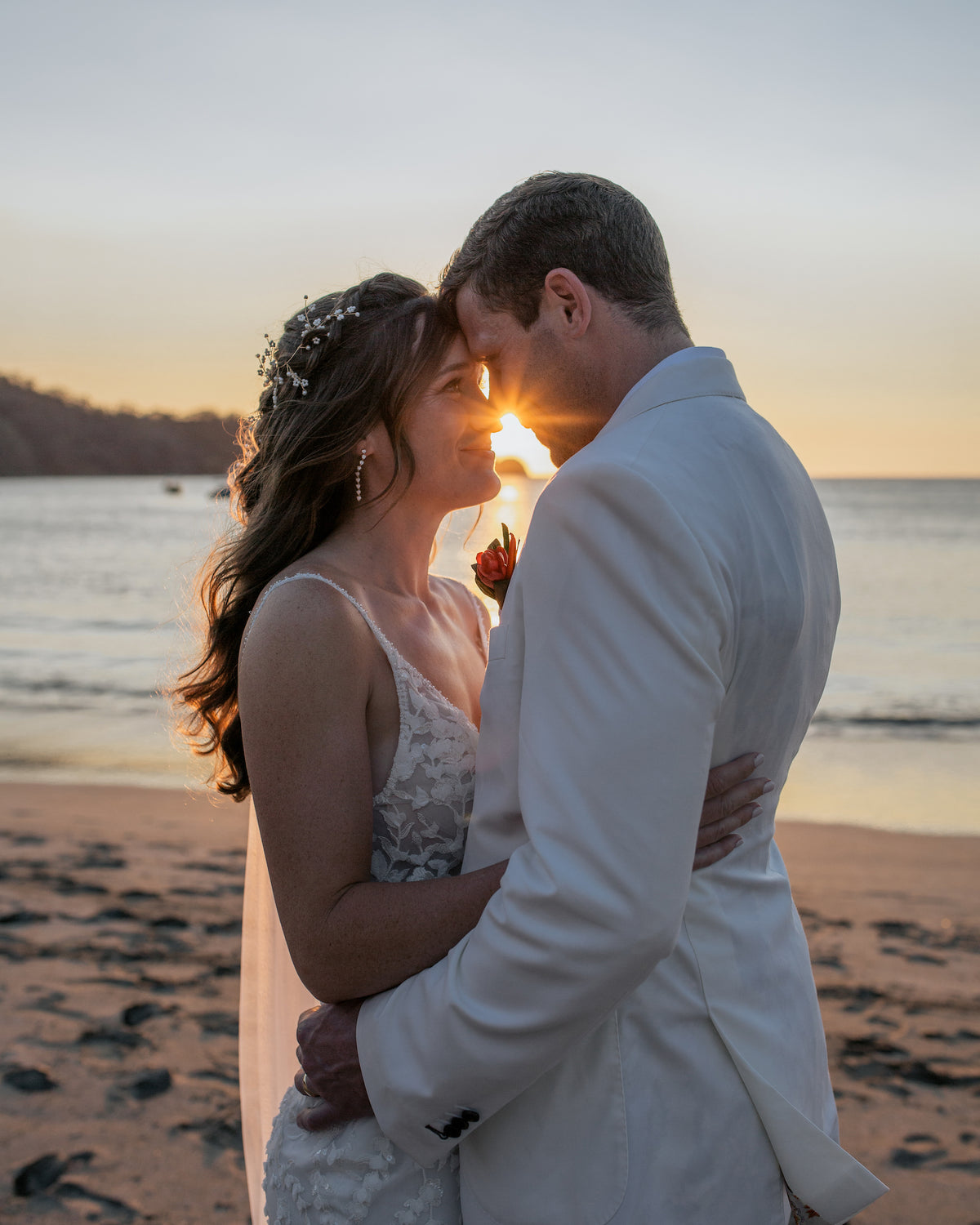 Bride and groom touch foreheads as the sun sets over the bay after their wedding