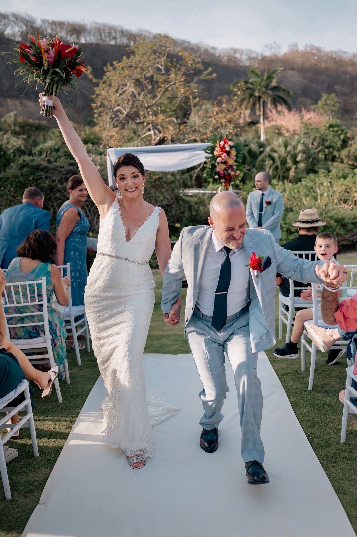 Newlyweds celebrate walking up the aisle, the bride raising her bouquet, at their beach wedding