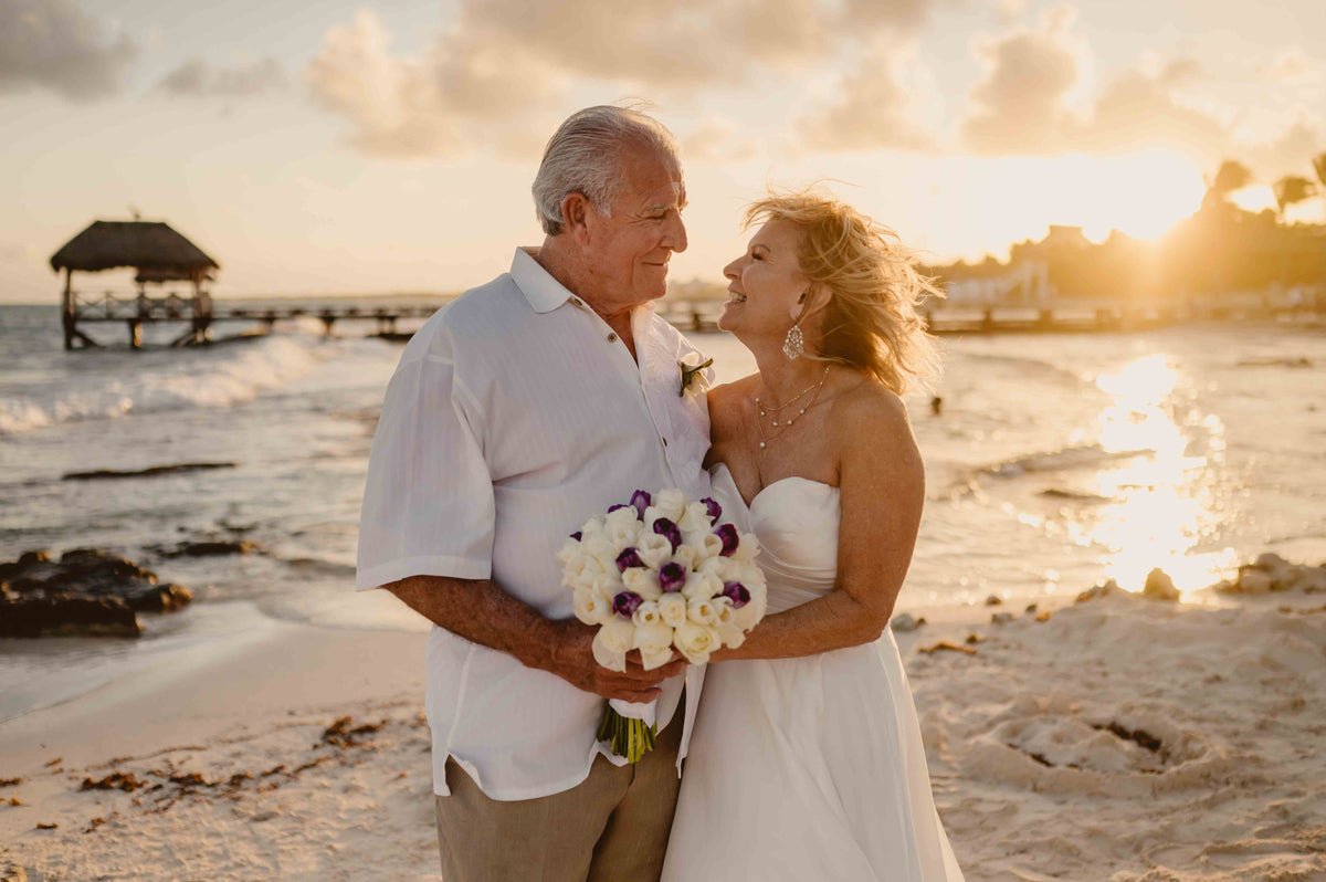 Photograph of a bride and groom holding flowers on the beach