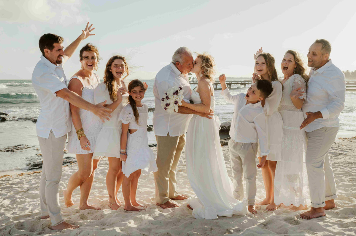 Photograph of bride and groom kissing as their family celebrates around them