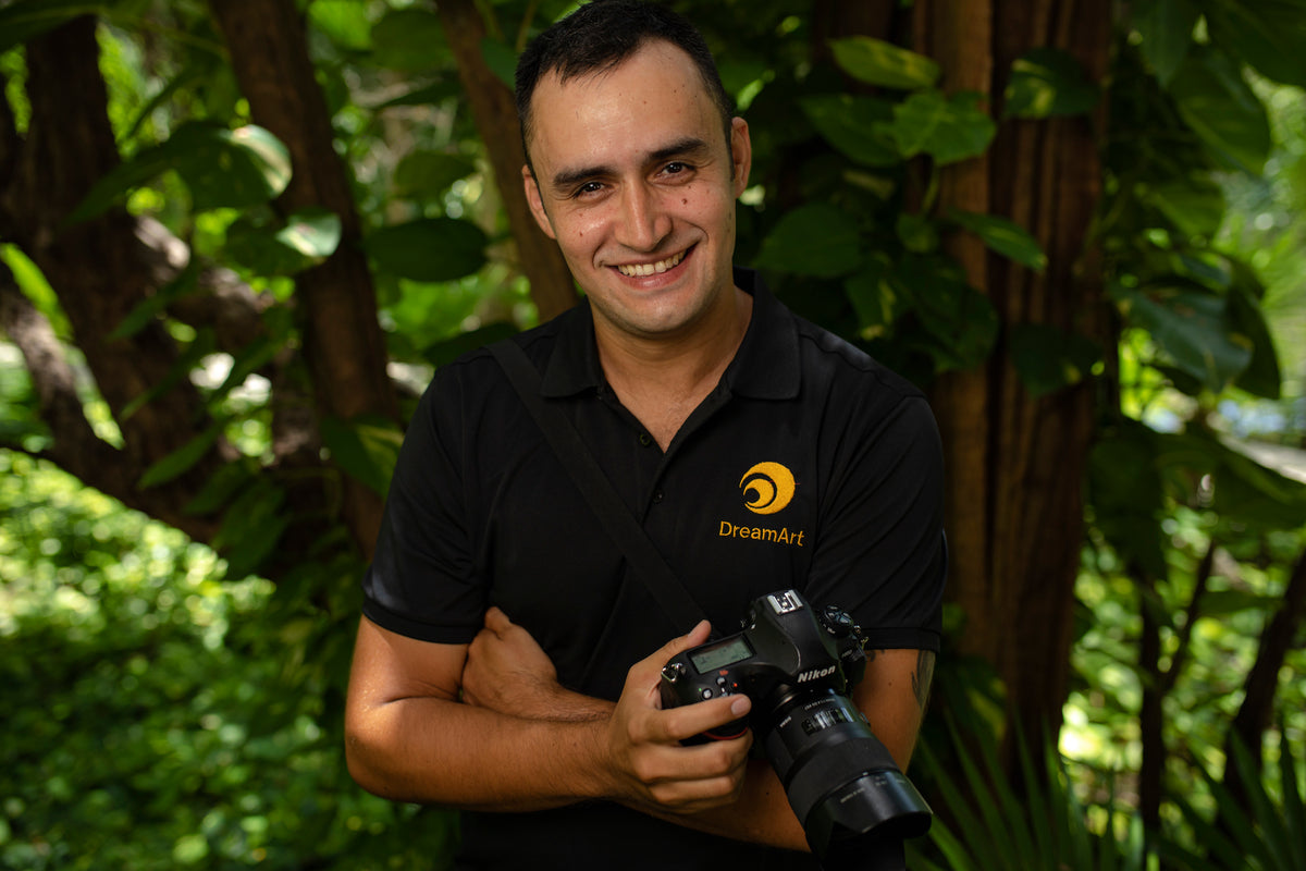 Smiling DreamArt hotel photographer holding a Nikon camera among jungle trees