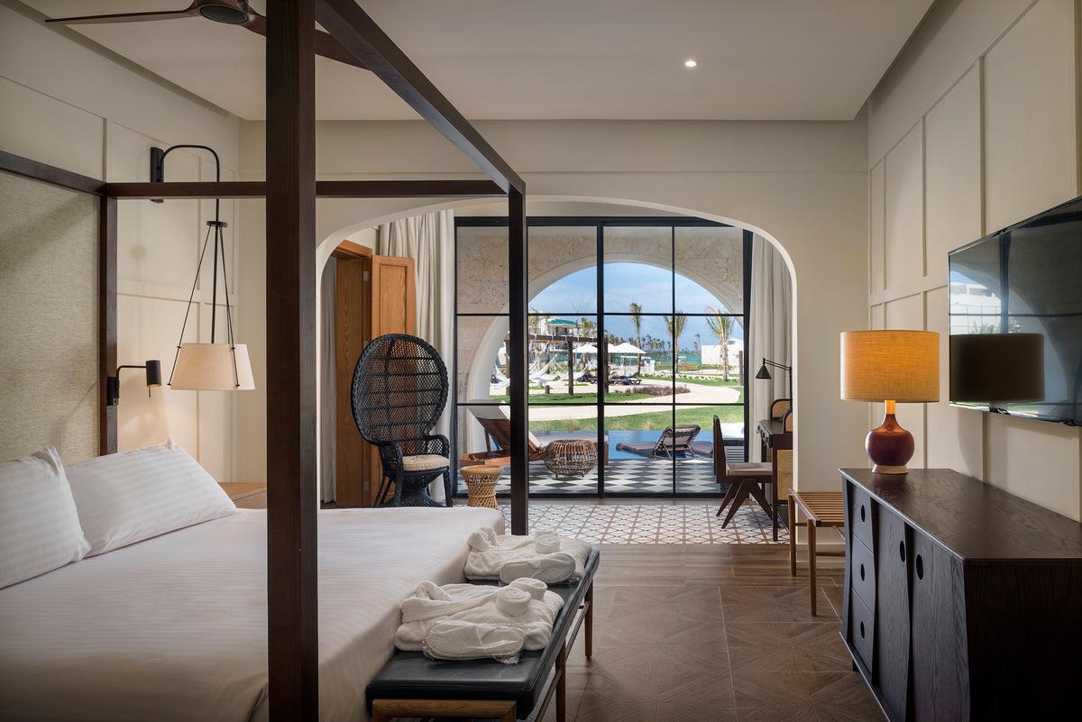 Bright four-poster suite with bathrobes on a bench and arched doors opening to the pool at Ocean El Faro