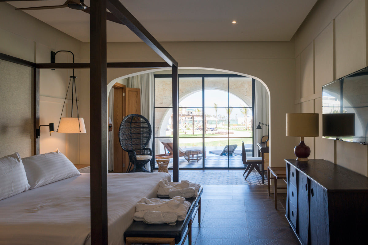 Hotel room photography of a four-poster bed, wicker peacock chair and garden terrace at Ocean El Faro