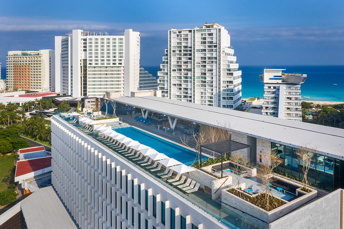 Hotel photography of a rooftop pool with white loungers above high-rise towers and the sea at Hilton