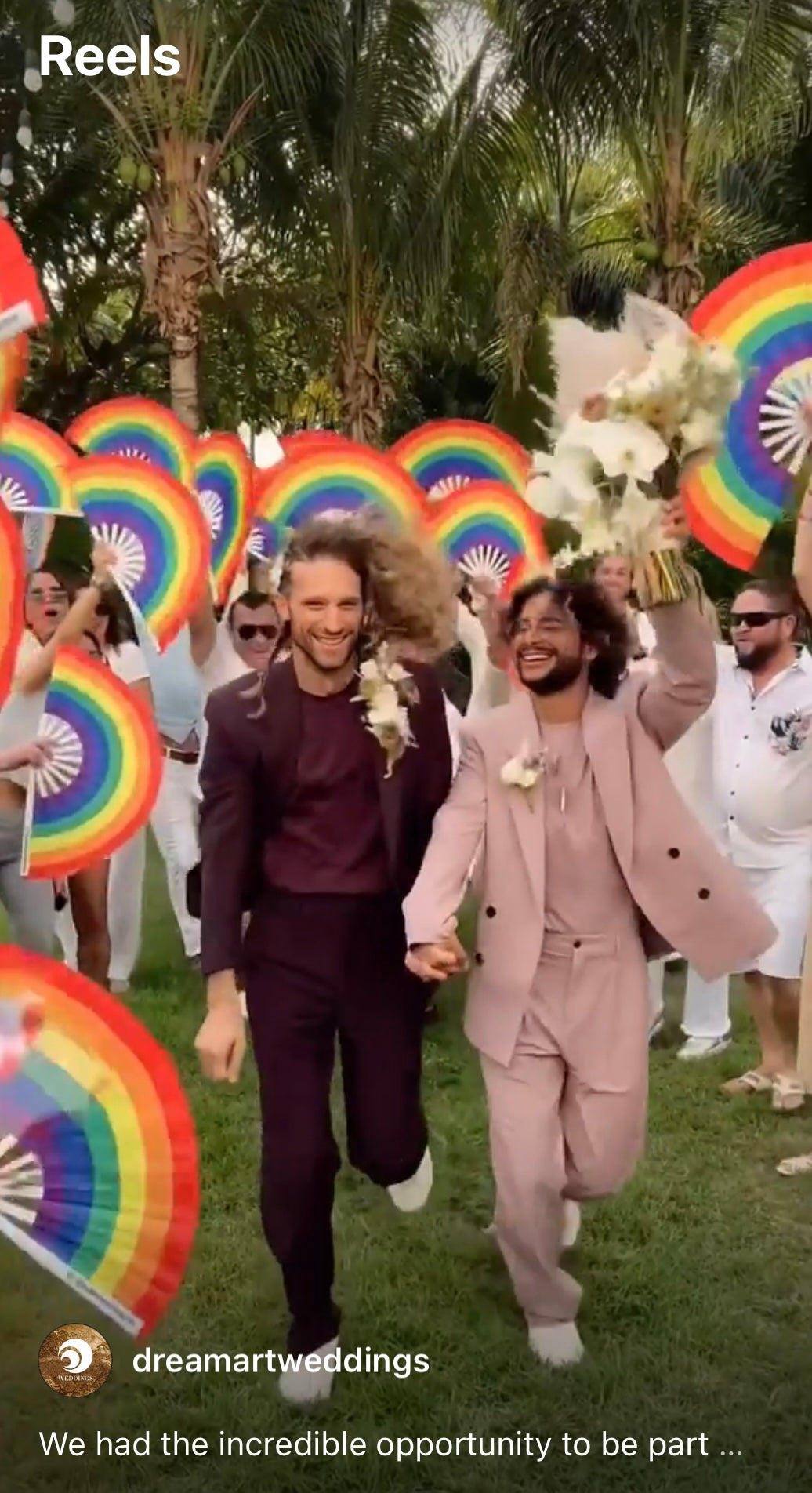 Wedding film reel cover of two grooms walking hand in hand as guests wave rainbow fans