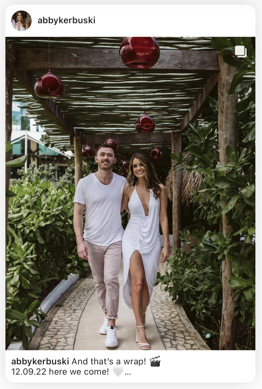 Instagram post of a couple walking under a pergola hung with red lanterns before their wedding