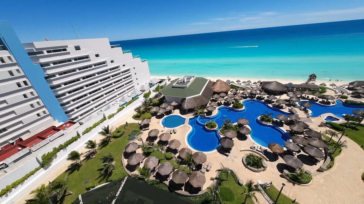 Aerial view of curved beachfront pools, palapas and turquoise sea at JW Marriott Cancun