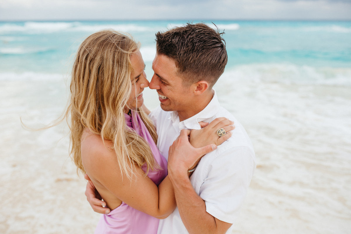 Couple embracing forehead-to-forehead on the beach with turquoise waves behind at JW Marriott Cancun