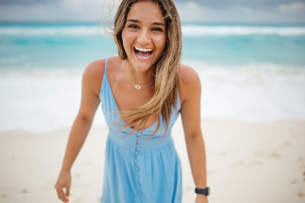 Woman in a light blue sundress laughing on the beach with turquoise water behind at JW Marriott Cancun