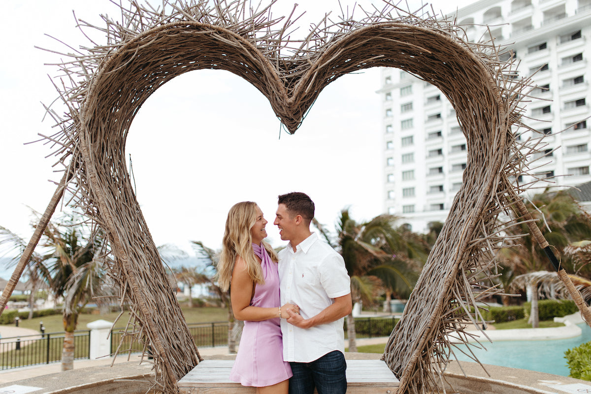 Couple facing each other under a heart-shaped twig arch with a resort tower behind at JW Marriott Cancun