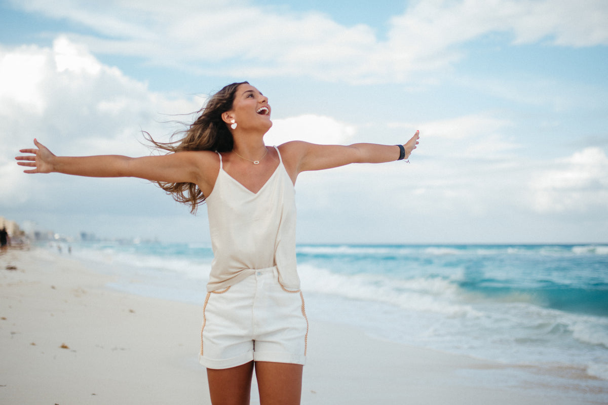 Woman in white on the beach with arms outstretched and the turquoise sea behind at JW Marriott Cancun