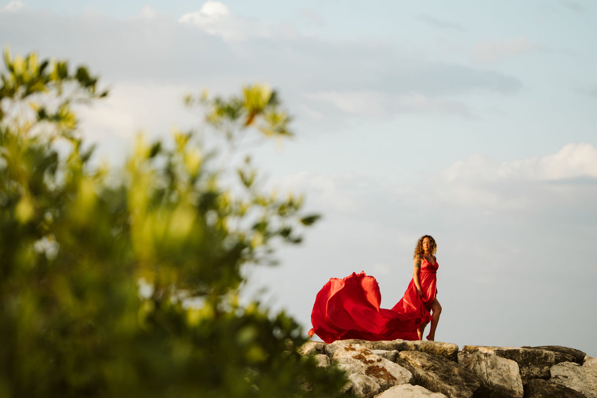Editorial-style photograph of a woman in a red dress posing on the beach rocks of Jamaica