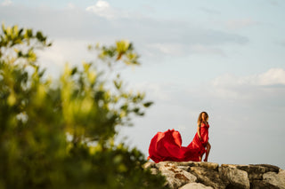 Editorial-style photograph of a woman in a red dress posing on the beach rocks of Jamaica 