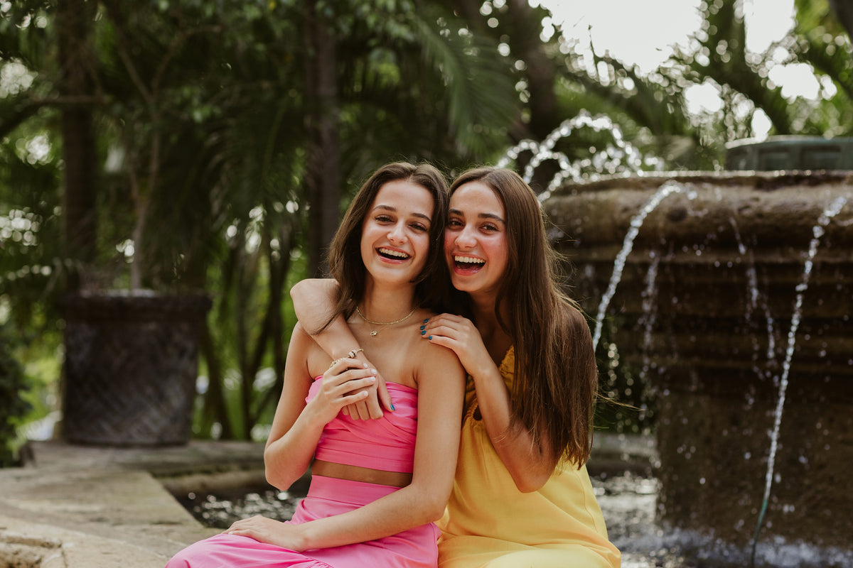 Two laughing sisters hug beside a stone fountain in a tropical garden at Kempinski Hotel Cancún