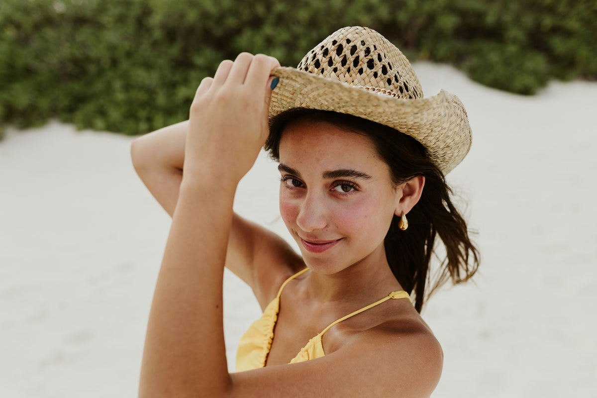 Smiling girl in a straw hat and yellow swimsuit poses on white sand at Kempinski Hotel Cancún