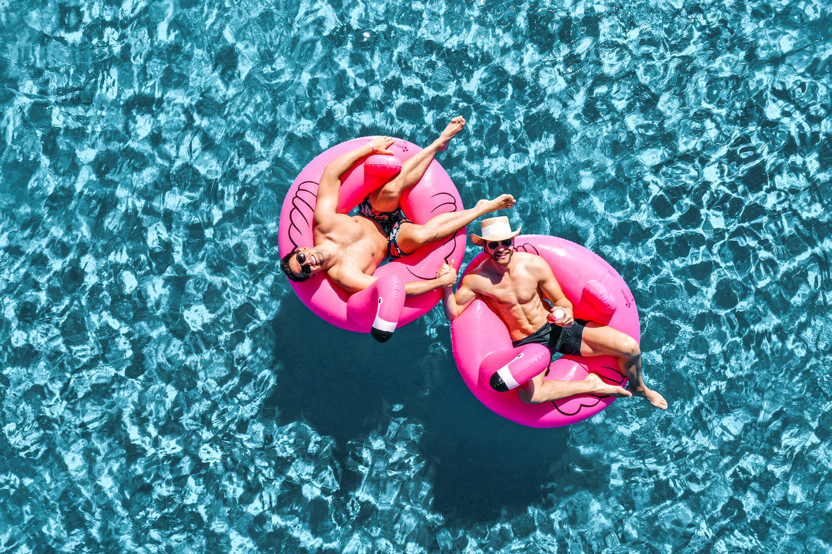 Aerial view of two men relaxing on pink flamingo pool floats in clear blue water