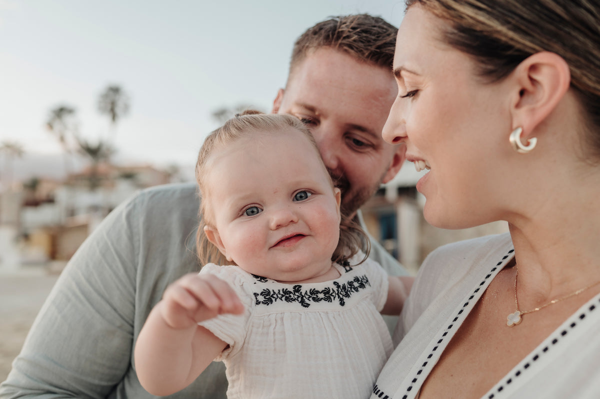 A close-up of a smiling baby held between a man and woman during a DreamArt lifestyle family session