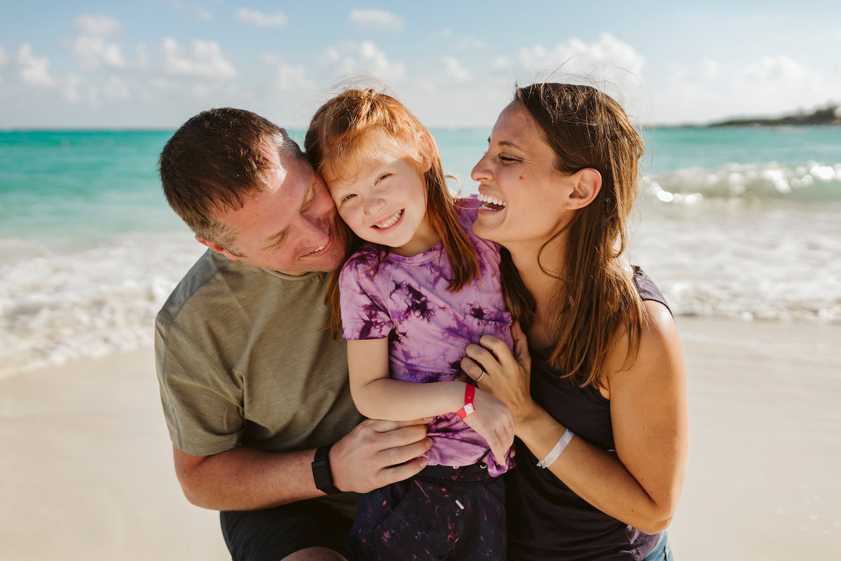 Two adults embrace a smiling child on the beach at Grand Fiesta Americana Coral Beach Cancún
