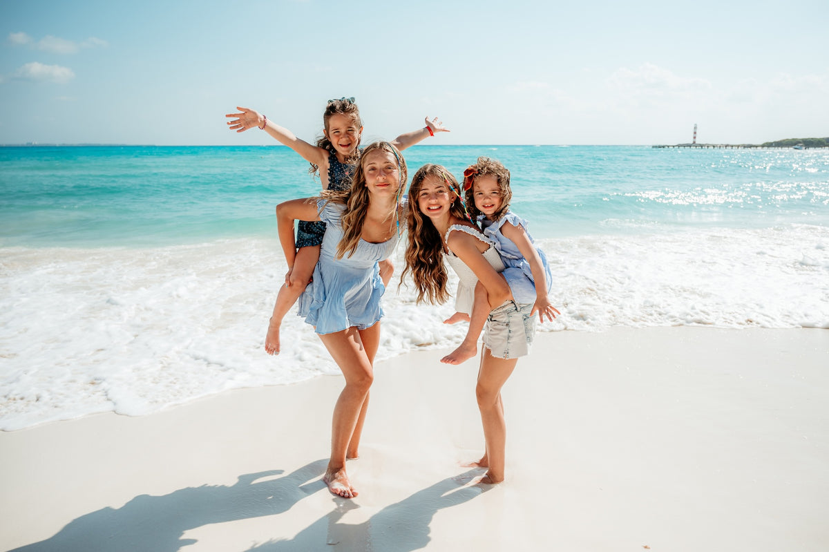 Two women give piggyback rides to young girls on the beach