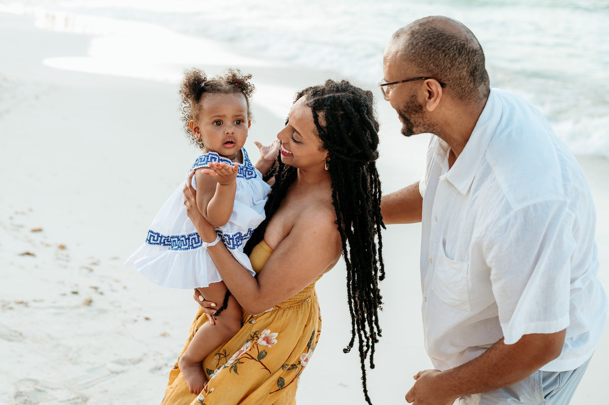 A woman holds a toddler while a man stands beside them on the beach