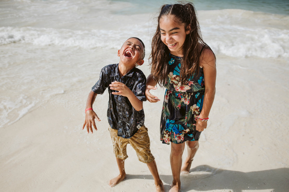 Two children laugh together on the beach at Grand Fiesta Americana Coral Beach Cancún, wet clothing and ocean waves behind them