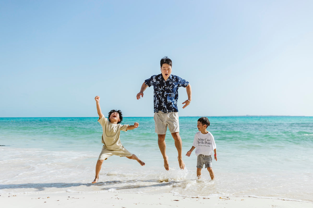 A man and two boys jump and play in shallow surf on the beach